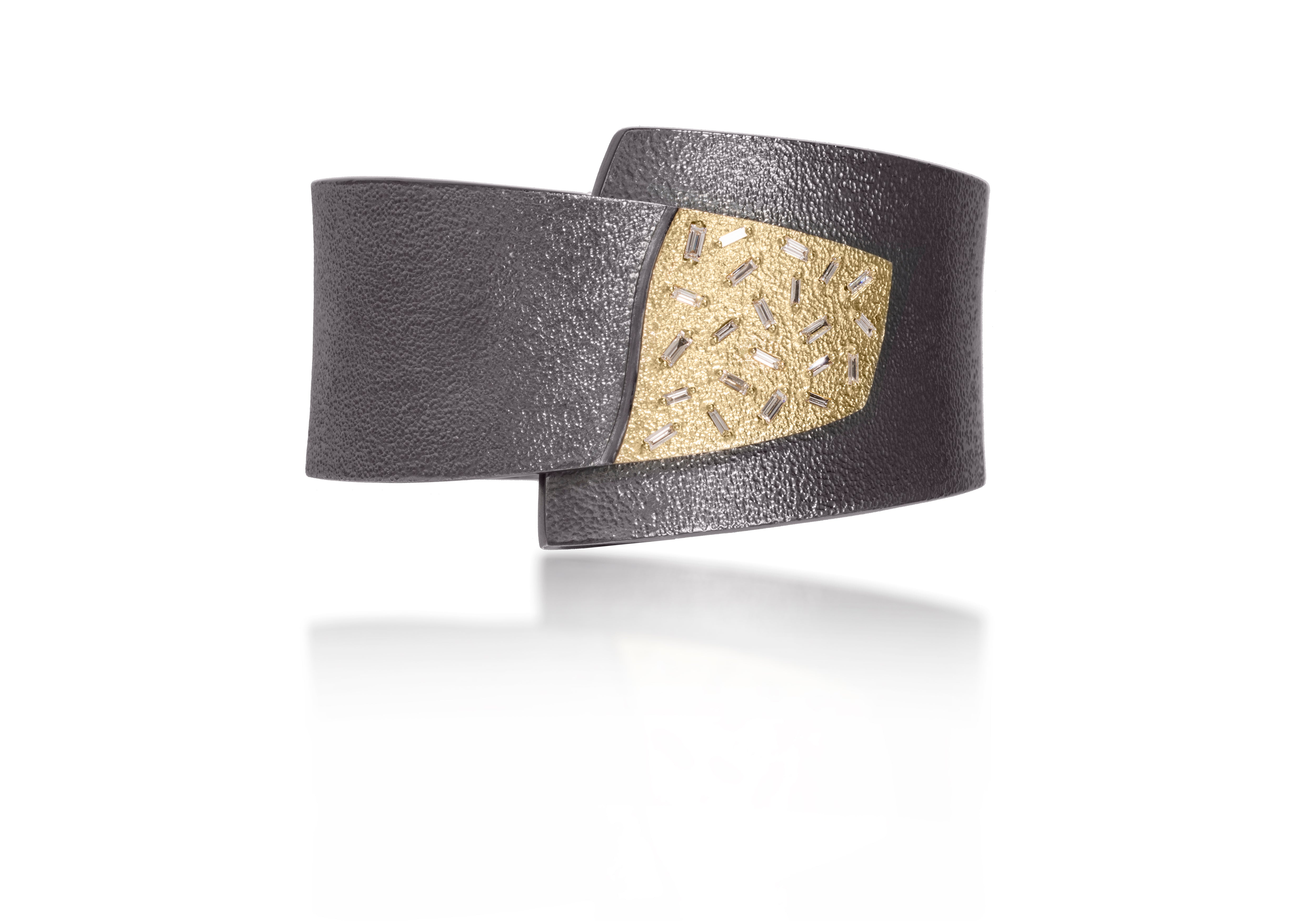 This cuff style bracelet in oxidized sterling and 18k gold is set with 22 white diamond baguettes. Richly textured, both the metal and diamonds shimmer in the light.  Bracelet features a spring hinge closure, making it extremely easy to put on and take off. 0.611 tcw.