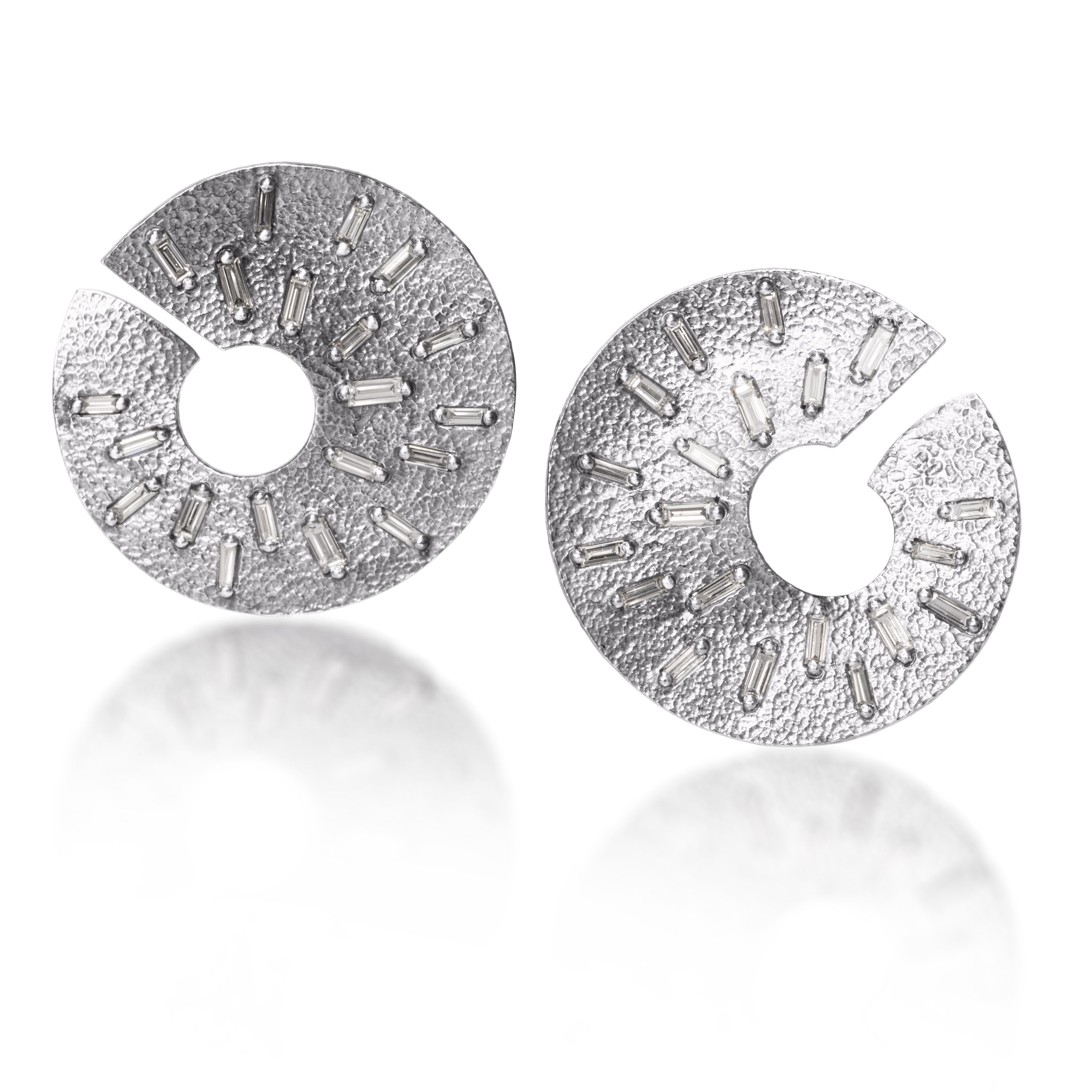 The smaller of two radiant styled earrings, each set with 21 white diamond baguettes. Richly textured and designed to three dimensionally wrap around from the front to behind the ear.  It is available in three color ways, oxidized silver, 18k gold and palladium.  1.176 tcw.