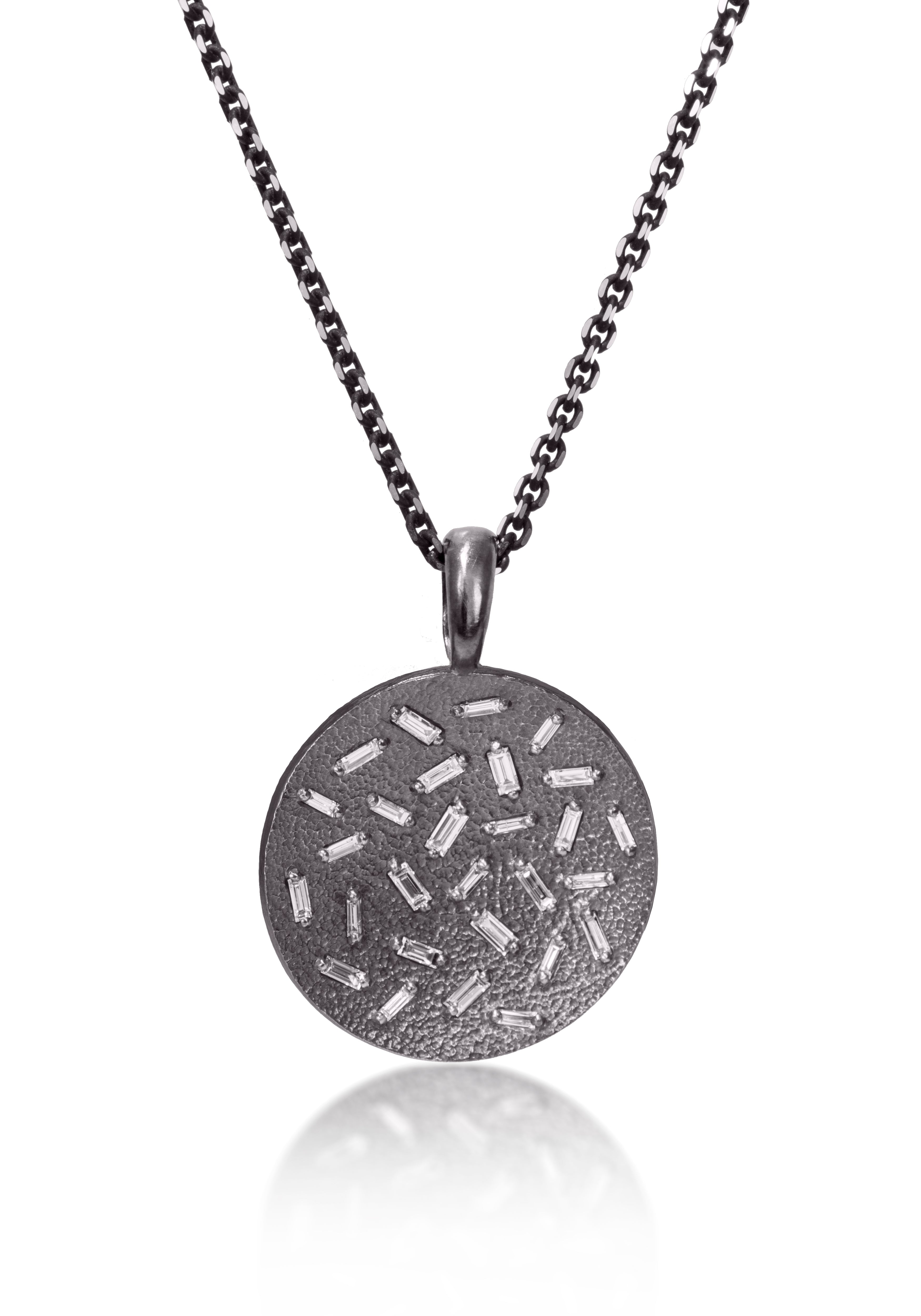 This large, radiant pendant is set with a stunning 28 white diamond baguettes. Richly textured to shimmer in the light, this piece is available in three color ways, oxidized silver, 18k gold and palladium. 0.773 tcw.