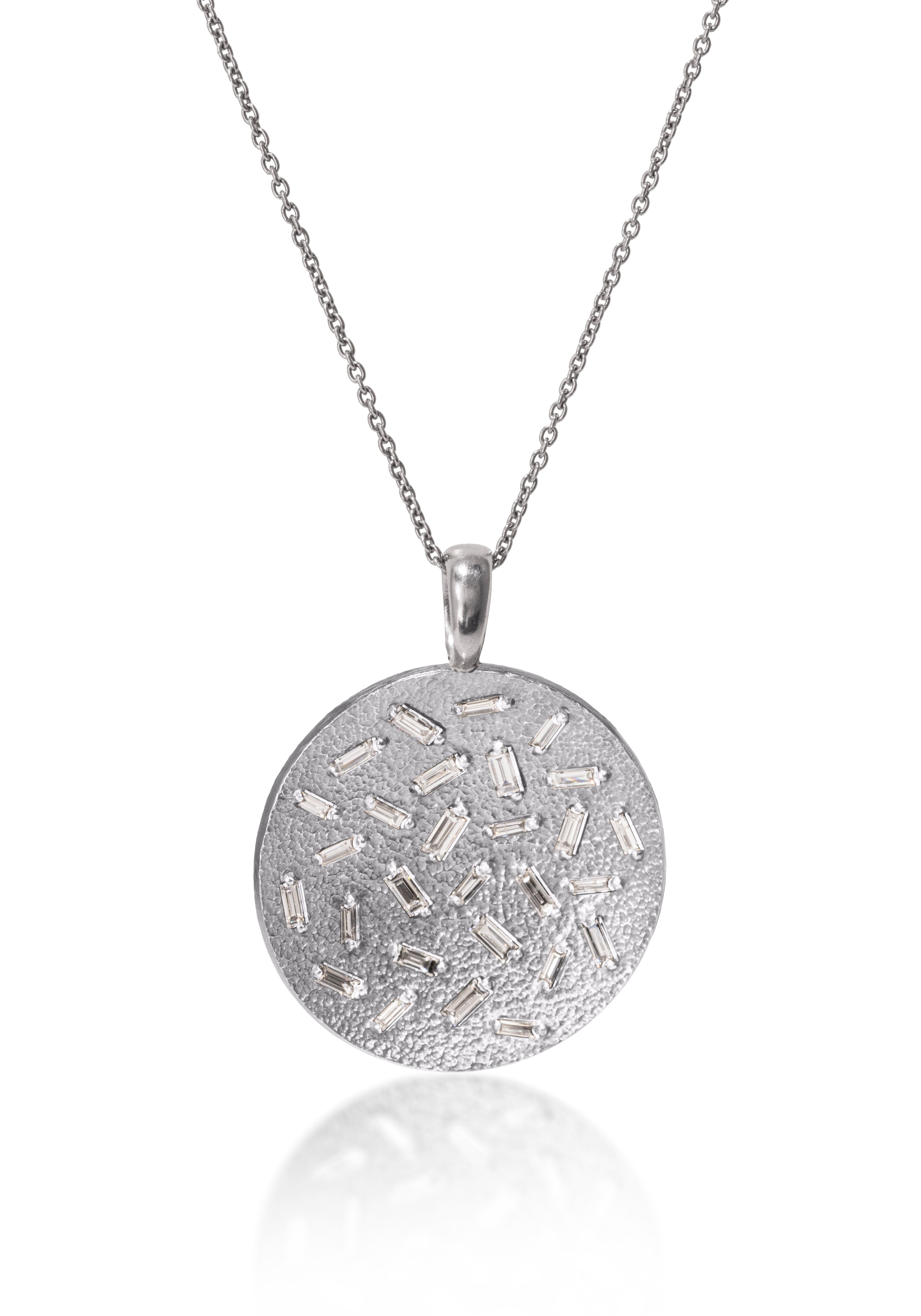 This large, radiant pendant is set with a stunning 28 white diamond baguettes. Richly textured to shimmer in the light, this piece is available in three color ways, oxidized silver, 18k gold and palladium. 0.773 tcw.