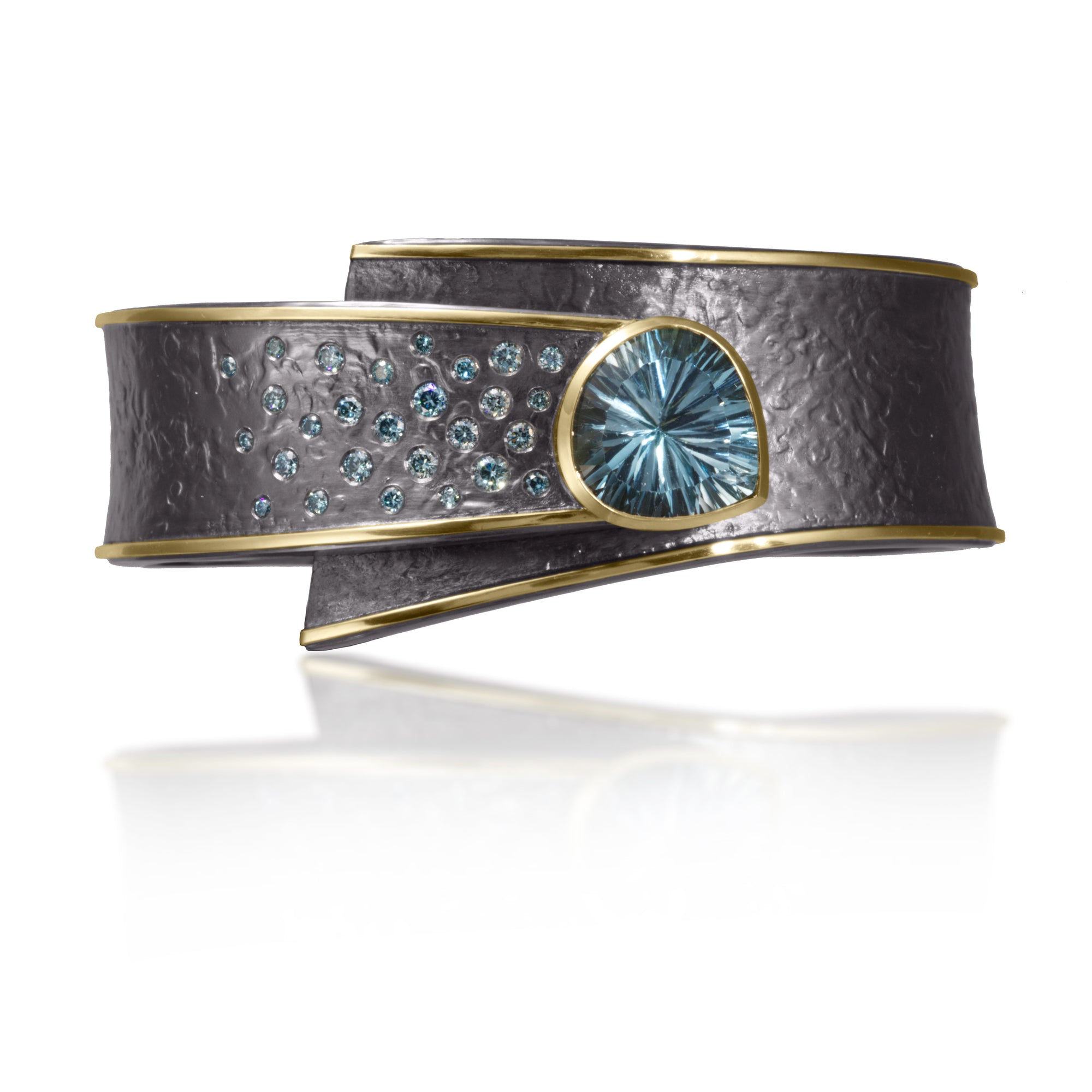 This one-of-a-kind Cyclone Cuff in 18k gold and oxidized silver is bezel set with a dramatic, convex-cut Blue Topaz and complimented by a spray of blue* diamonds.  A hinge on the back side of this tapered cuff allows it to fully open, making it incredibly easy to put on and off with one hand. Wide, wrap-around style cuff, hand fabricated, spring steel hinge, hammer textured.  Blue Topaz 9.65 ct. *color treated blue diamonds 0.78 tcw.H:27 mm x D:4 mm