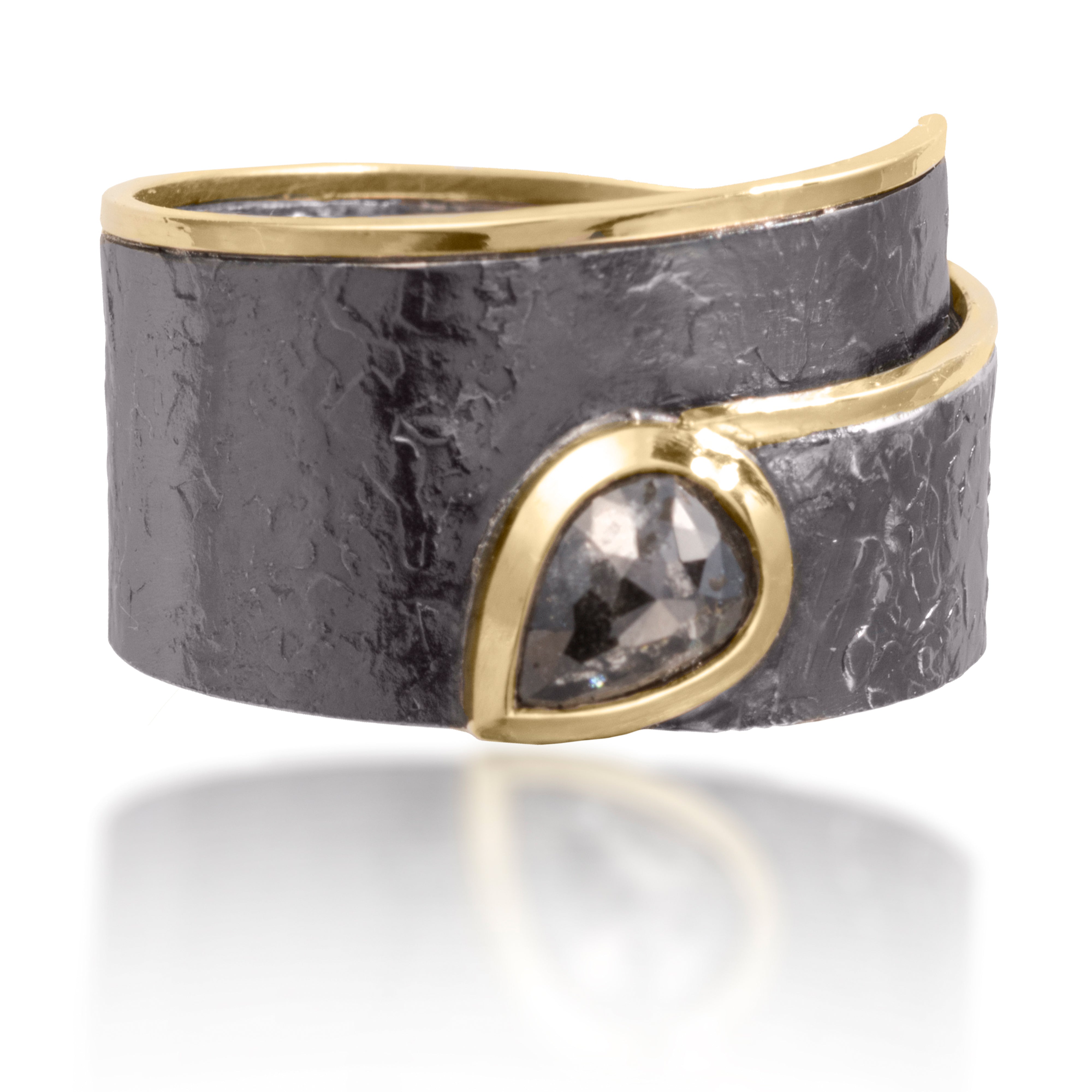 This simple, yet distinctive ring in 18k gold and oxidized silver features a bezel set center tear drop, rustic diamond. It is hand fabricated and hammer textured. Available in various widths and colors.