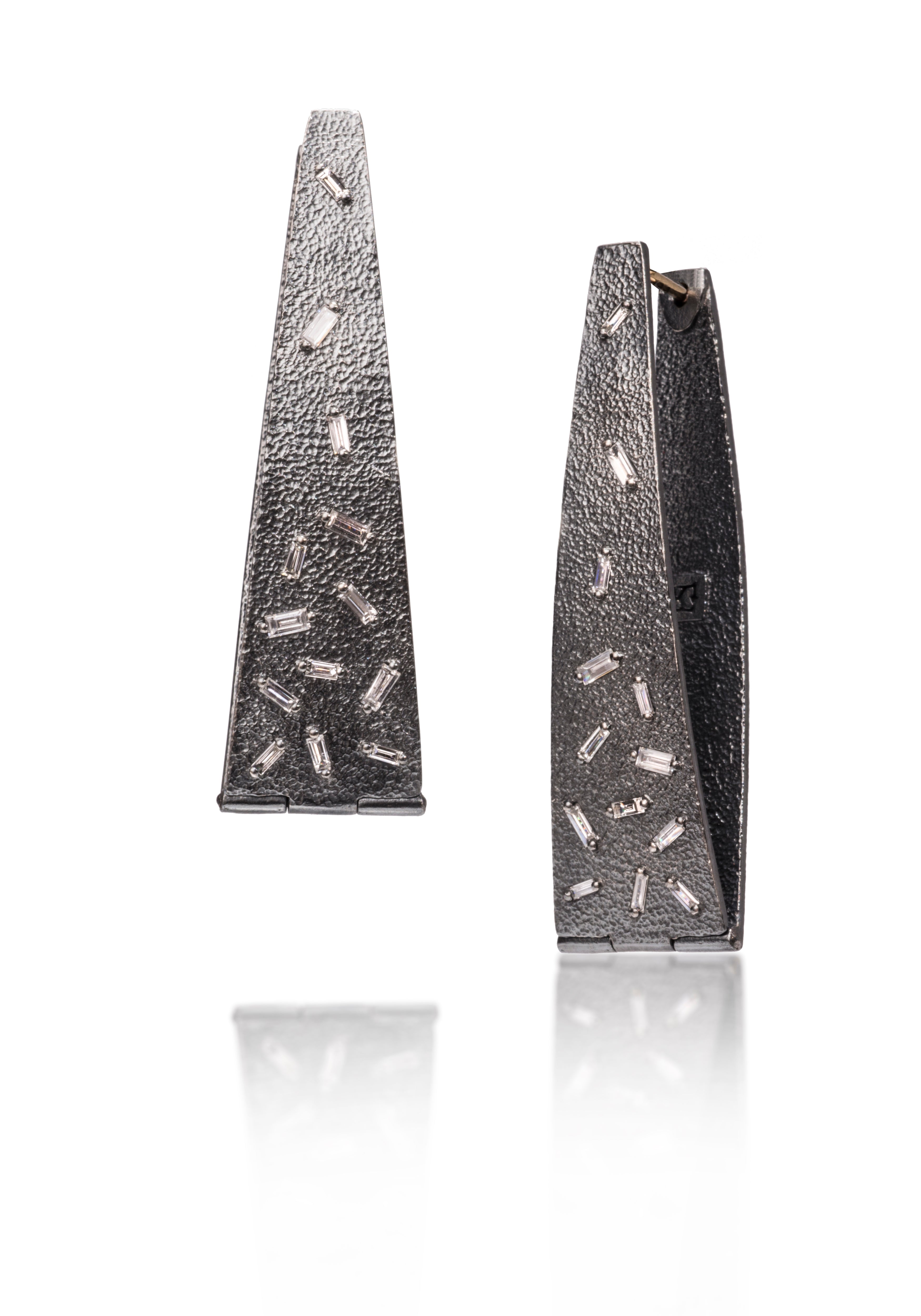 These long, elegant flare, huggie style earring are each set with 13 white diamond baguettes. Richly textured, this full size version is only available in oxidized silver.   0.812 tcw.