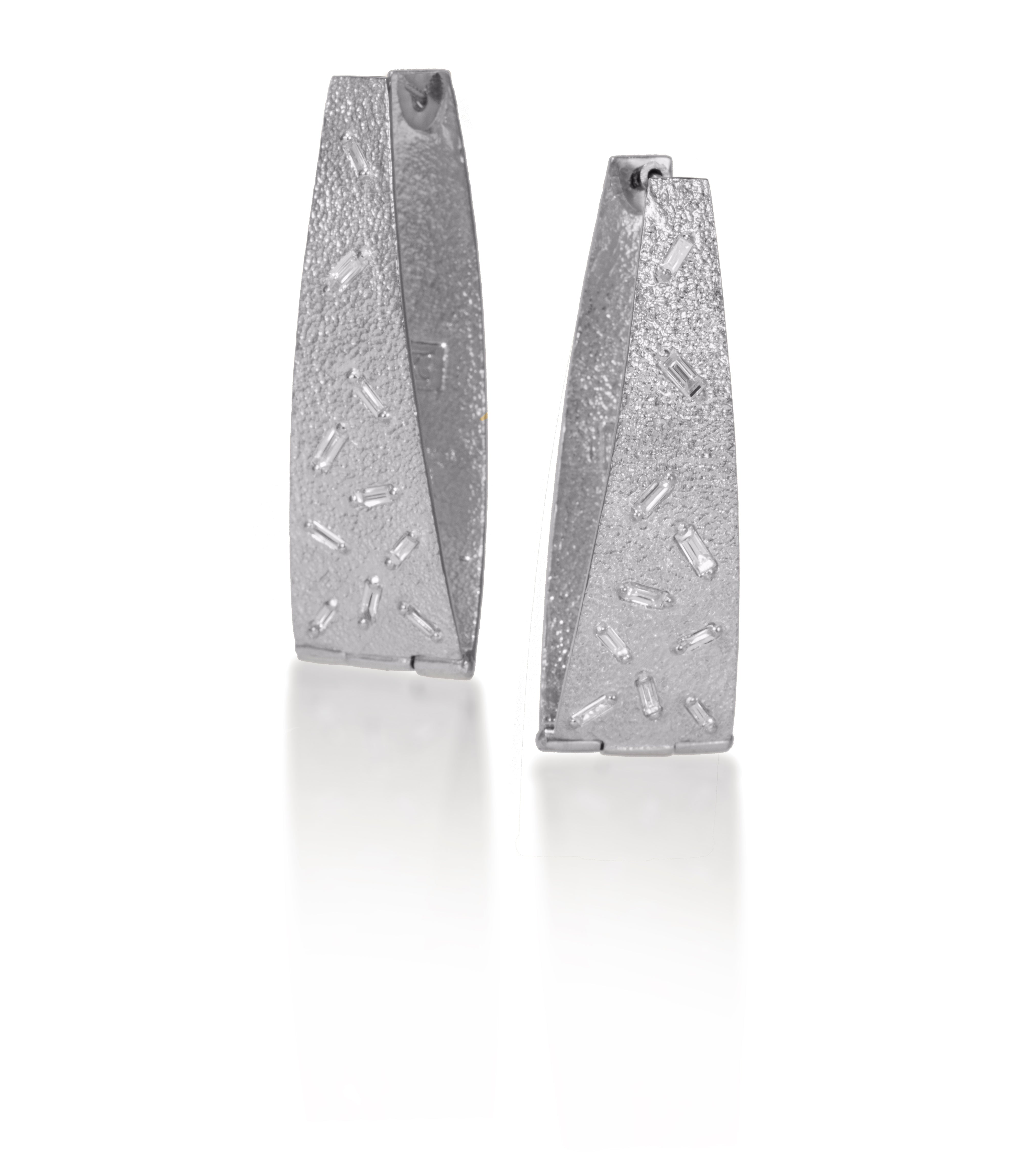 These long, elegant flare, huggie style earring are each set with 10 white diamond baguettes. Richly textured, it is available in three color ways, oxidized silver, 18k gold and palladium.   0.546 tcw.