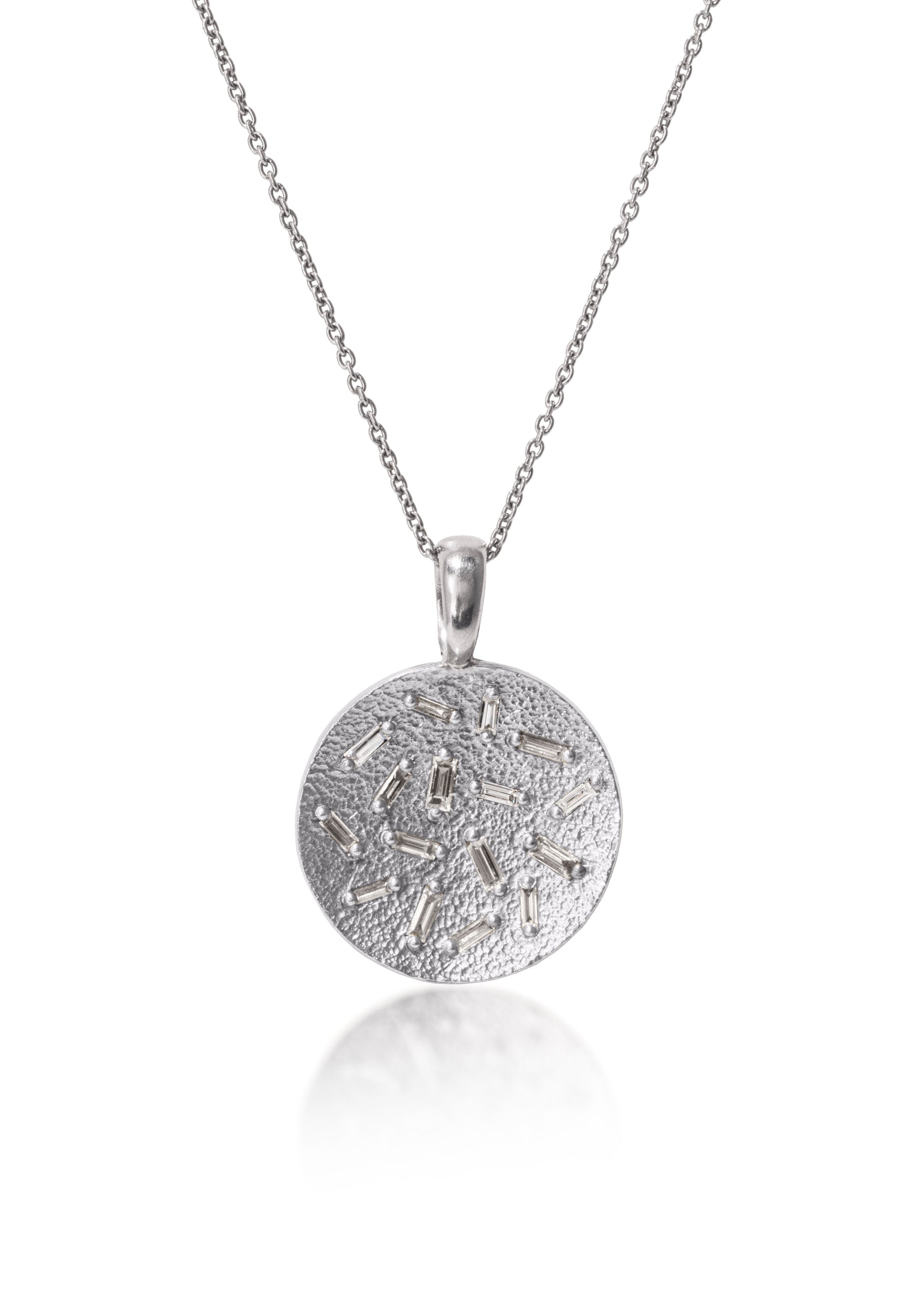 This radiant, medium size circular pendant is set with 16 white diamond baguettes. Richly textured to shimmer in the light, this piece is available in three color ways, oxidized silver, 18k gold and palladium.  0.435 tcw.