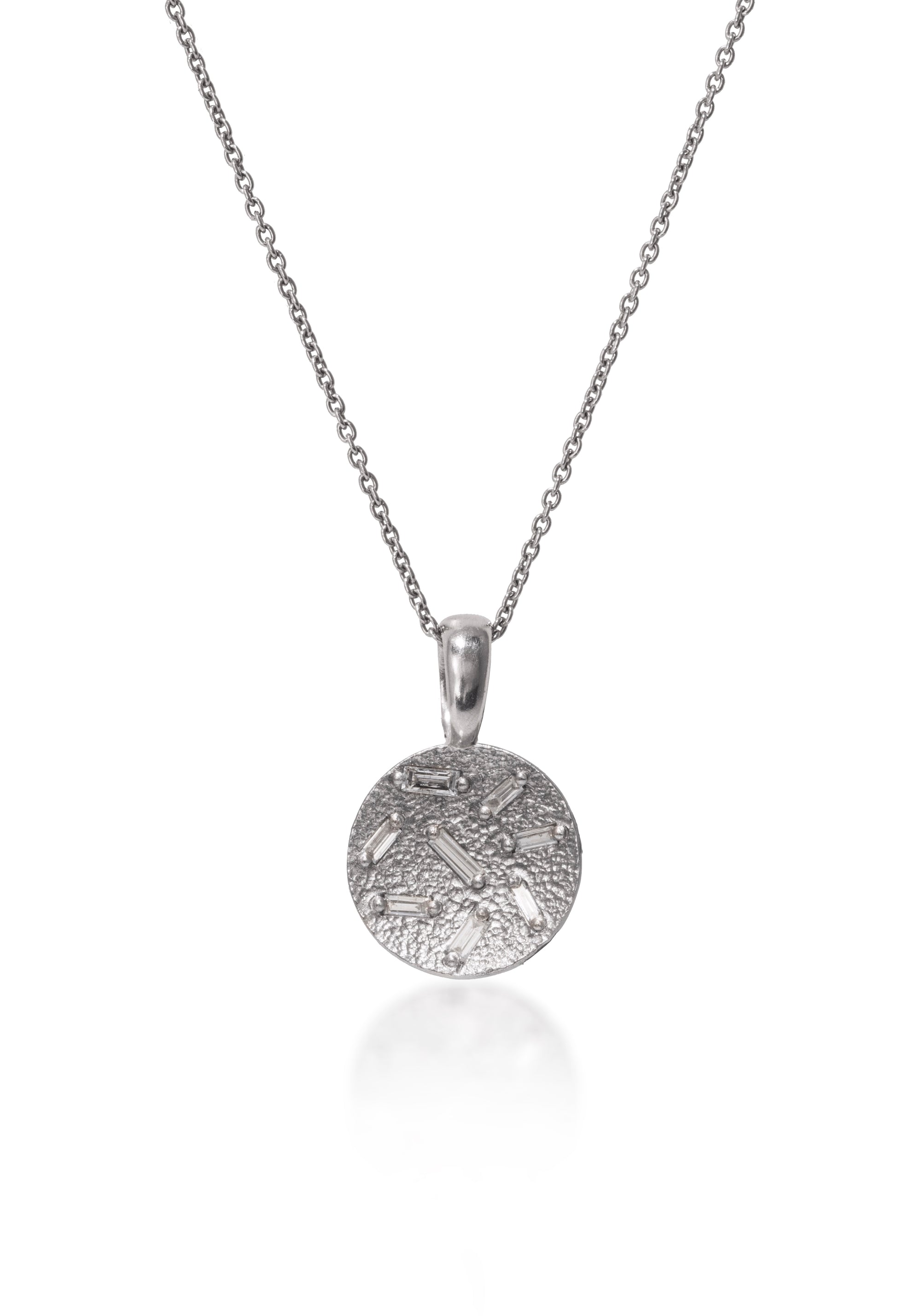 This stunning, small circular pendant is set with 8 white diamond baguettes. Richly textured to shimmer in the light, this piece is available in three color ways, oxidized silver, 18k gold and palladium.  0.227 tcw.